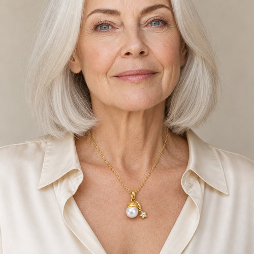 Woman wearing the Agnes gold cap pearl and star charm pendant necklace at the sternum with a navy sweater
