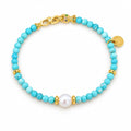 Dorotea turquoise-blue bead bracelet with a single white freshwater pearl and polished clasp section, flat lay on pale green