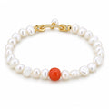 Eugenia white baroque freshwater pearl bracelet with one red-orange accent bead, flat lay on pale green