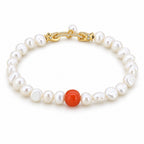 Eugenia white baroque freshwater pearl bracelet with one red-orange accent bead, flat lay on pale green