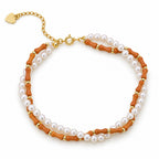 Francesca double-strand bracelet with white pearls and orange-brown bamboo-shaped beads, flat lay on cream