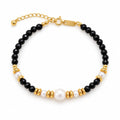 Martina black faceted bead bracelet with a central white freshwater pearl and polished spacers, flat lay on a printed page