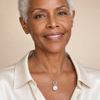 Woman wearing the Nora pavé circle pearl pendant necklace at the sternum with a black crew-neck top