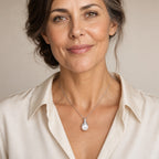 Woman wearing the Verity polished tulip cap pearl pendant necklace at the sternum with a gray sweater